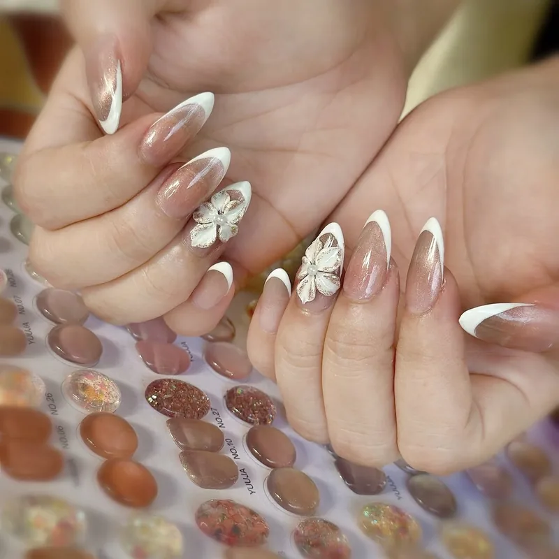 Long almond nails with white tips and a sculpted 3D flower