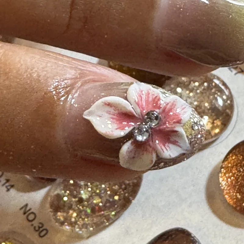 Close-up of a sculpted 3D flower with a rhinestone centre over gold glitter